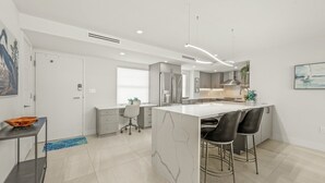 A modern kitchen with a central island, bar stools, and a dining area. - Crystal Sands Tower Unit 909 - Beachfront (Sarasota)