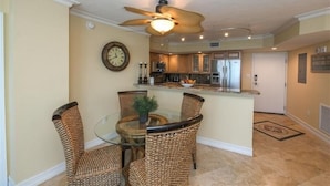 A dining area with wicker chairs, a glass table, and a ceiling fan. - Crystal Sands Tower Unit 703 - Beachfront (Sarasota)