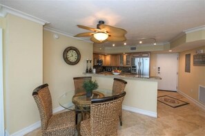 A dining area with wicker chairs, a glass table, and a ceiling fan. - Crystal Sands Tower Unit 703 - Beachfront (Sarasota)