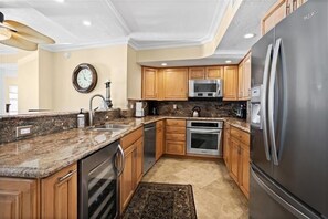 A kitchen with granite countertops, stainless steel appliances, wooden cabinets, and a clock on the wall. - Crystal Sands Tower Unit 703 - Beachfront (Sarasota)
