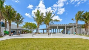 A modern building with a covered outdoor area, palm trees, and a grassy lawn. - Crystal Sands Villa 1 - Private Beach (Sarasota)