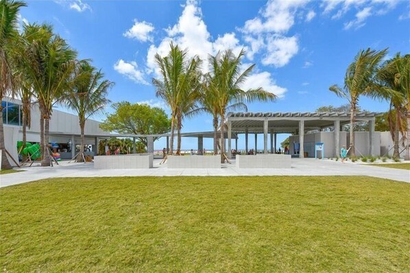 A modern building with a covered outdoor area, palm trees, and a grassy lawn.