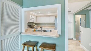 A kitchen with a built-in island, white cabinets, and a view into the adjacent dining area. - Crystal Sands Villa 1 - Private Beach (Sarasota)