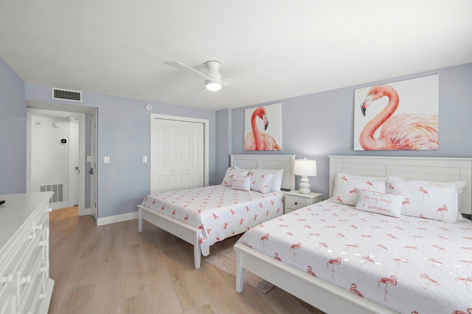 A bedroom with two beds, a ceiling fan, and a door leading to another room.