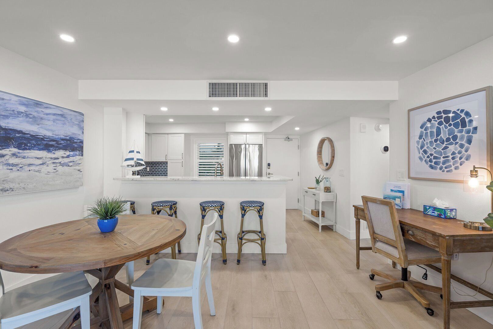 Une cuisine moderne avec des meubles blancs, un îlot central et un coin repas comprenant une table et des chaises en bois.