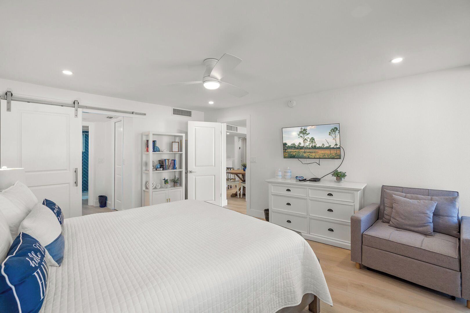 A bedroom with a bed, a dresser, a TV, and a seating area.