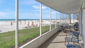 Uitzicht op het strand vanaf een overdekt terras met buitenmeubilair.