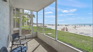 Een overdekt balkon met uitzicht op een strand, zitplaatsen buiten en een heldere lucht.