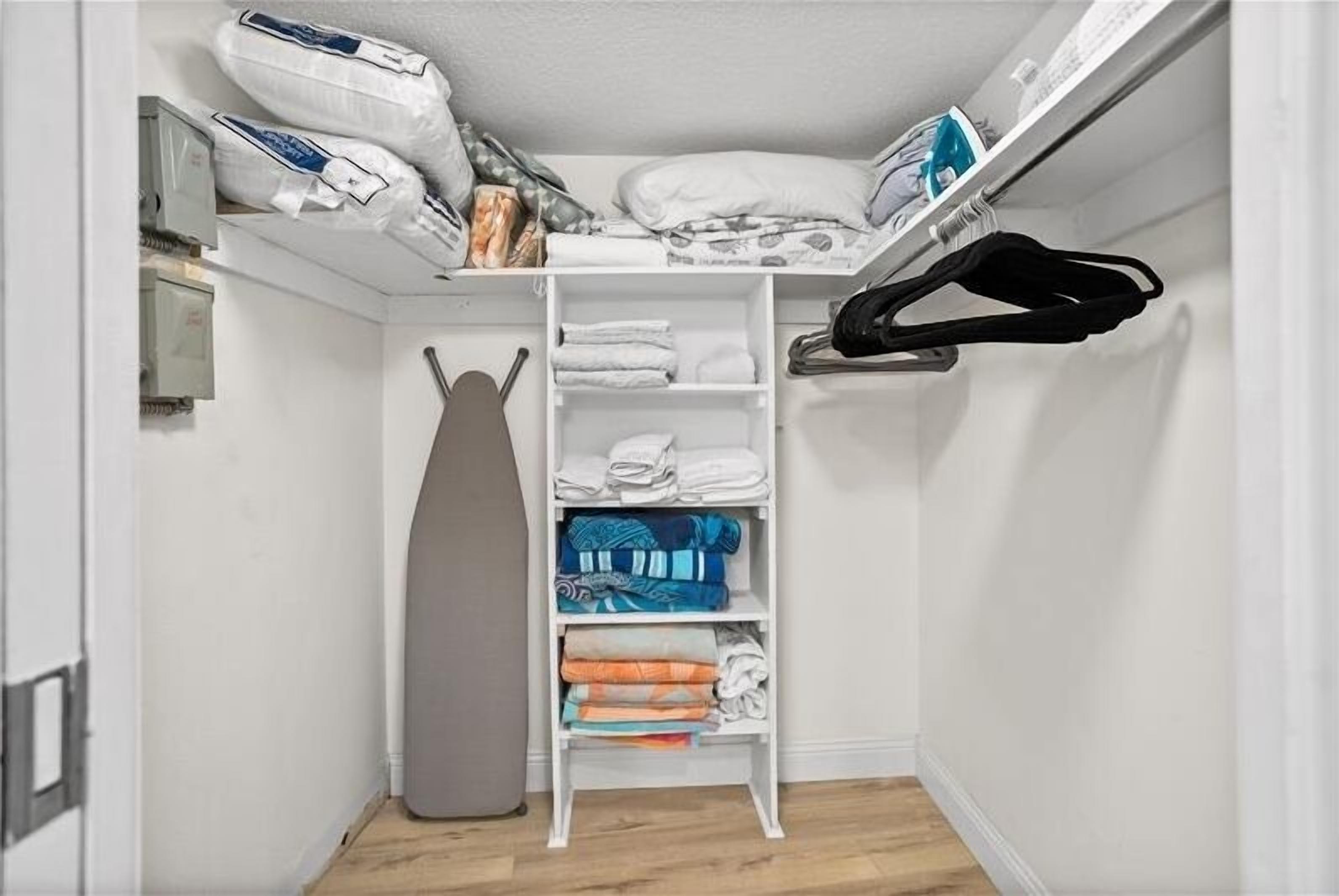 A neatly organized closet with shelves, a hanging rack, and an ironing board.