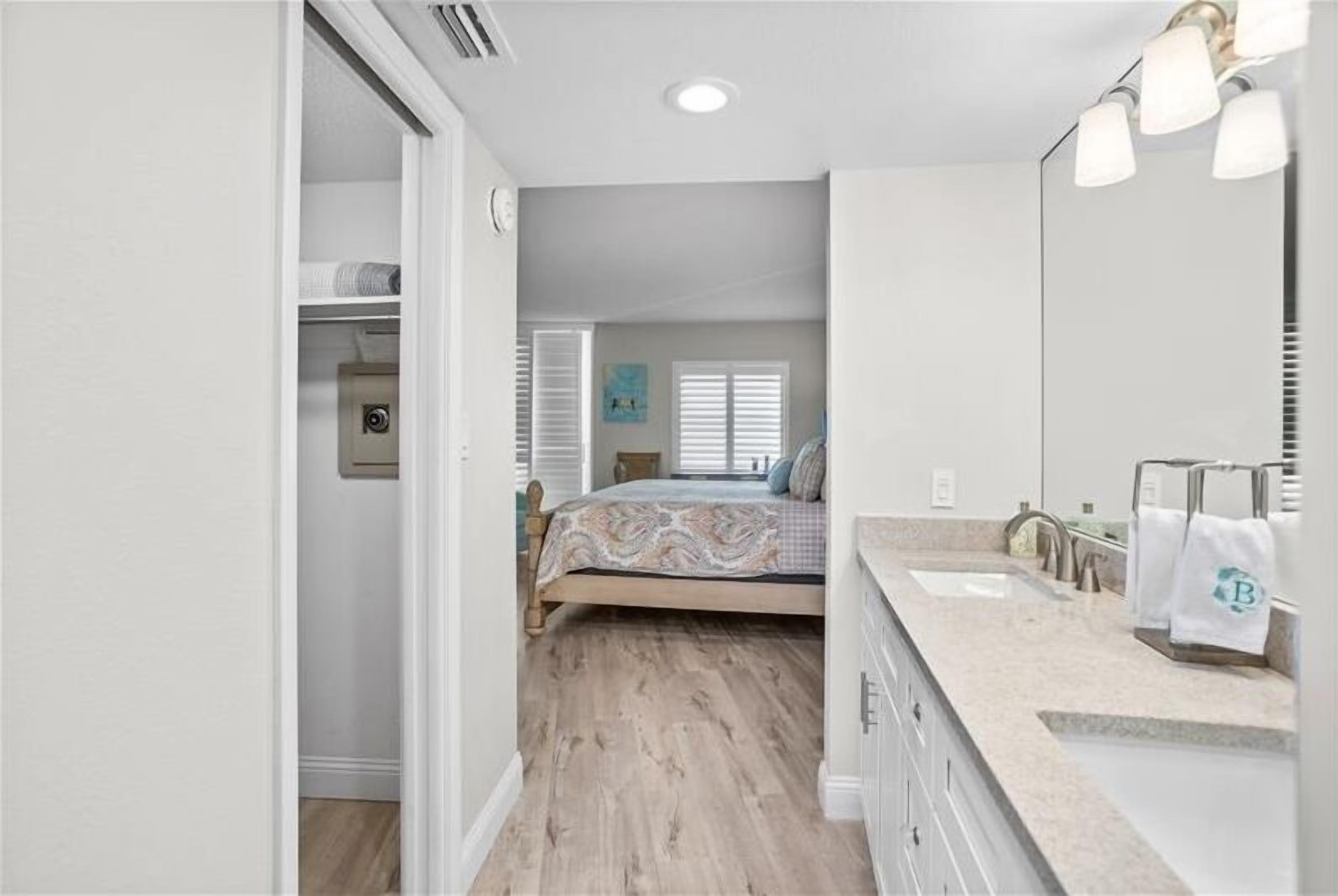 A bedroom with a bed, a bathroom with a sink and mirror, and a hallway leading to another room.