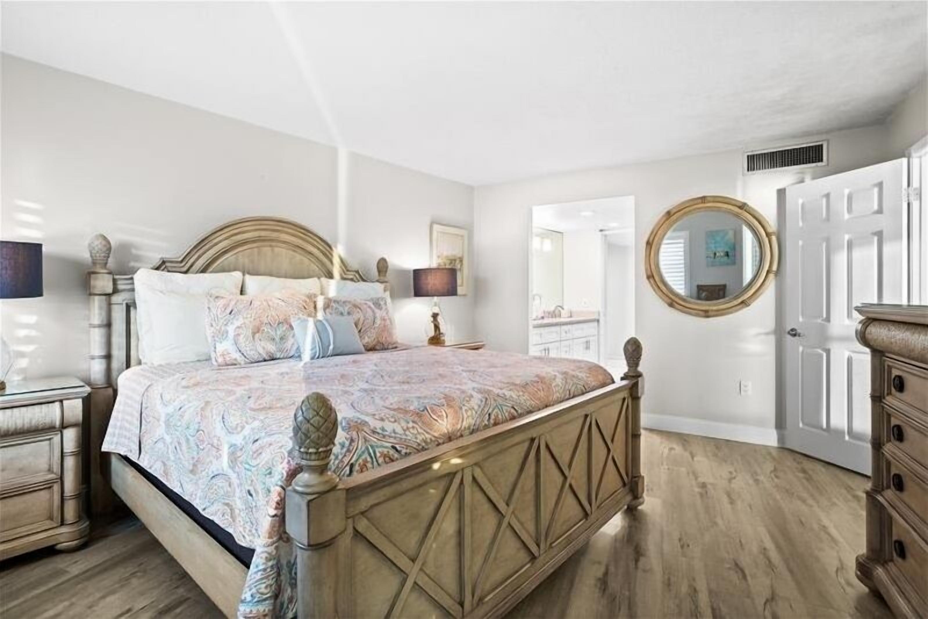 A bedroom with a bed, bedside tables, a dresser, a mirror, and a door.