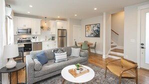 A modern apartment with a grey sofa, a dining area, a kitchen, and a staircase. - WeHo 3 Story Townhome 3 of 4 w/ Balcony WALKABLE! 8 mins drive to BRDWY!  (Nashville)