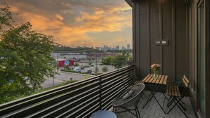 A balcony with a table and chairs, overlooking a cityscape with a sunset sky. - WeHo 3 Story Townhome 3 of 4 w/ Balcony WALKABLE! 8 mins drive to BRDWY!  (Nashville)