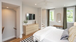Un dormitorio con cama, cómoda, televisión, espejo y ventana con cortinas.