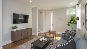 Una sala de estar moderna con un televisor de pantalla plana, un mueble de madera, un sofá gris y una mesa de centro con objetos decorativos.