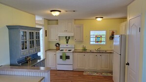 Cocina compacta con armarios blancos, estufa, refrigerador y ventana con diseño de vitral.