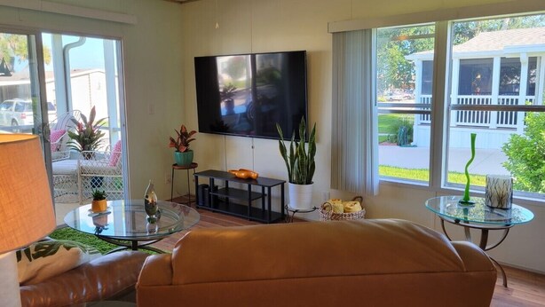 Una sala de estar con un sofá, una mesa de centro de vidrio, un televisor y un ventanal con vistas al exterior.