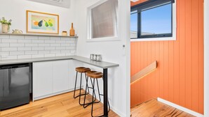 A modern kitchen with white cabinetry, a black dishwasher, and a wooden bar stool. - Apartment Studio 6: In The Heart of Torquay (Torquay)