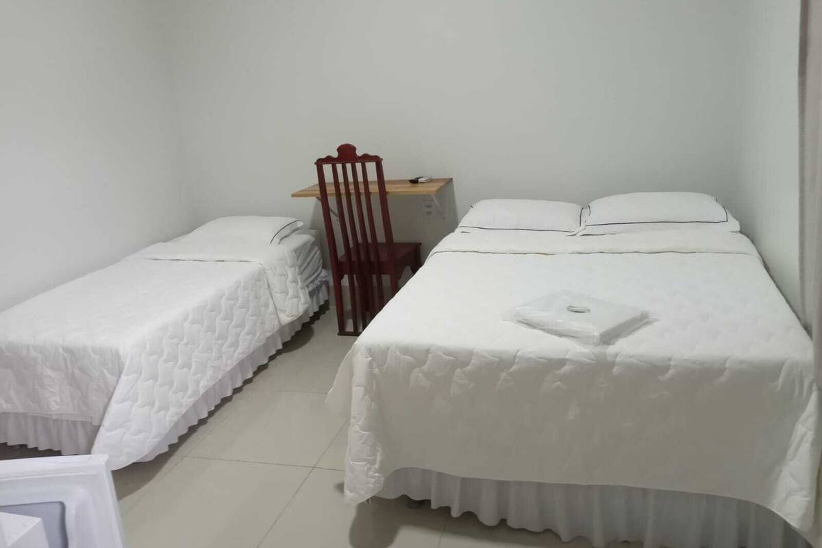 A room with two single beds, a wooden chair, a small table, and a white wall.