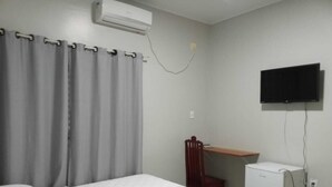 A bedroom with a bed, a desk, a chair, a TV, and a refrigerator.