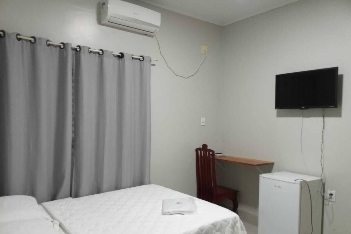 A bedroom with a bed, a desk, a chair, a TV, and a refrigerator.