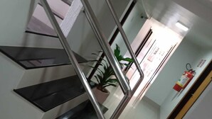 Una escala moderna amb baranes metàl·liques i graons negres, que condueix a un espai amb una planta i un extintor a la paret.