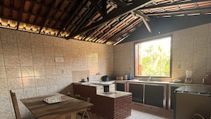 A compact kitchen with a wooden table and bench, a brick oven, and a window with a view of greenery. - Sítio Tôa Tôa - Rio Piracicaba (MG) (Rio Piracicaba)