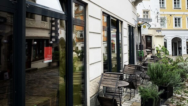 A café with outdoor seating, large windows, and a cobblestone patio.