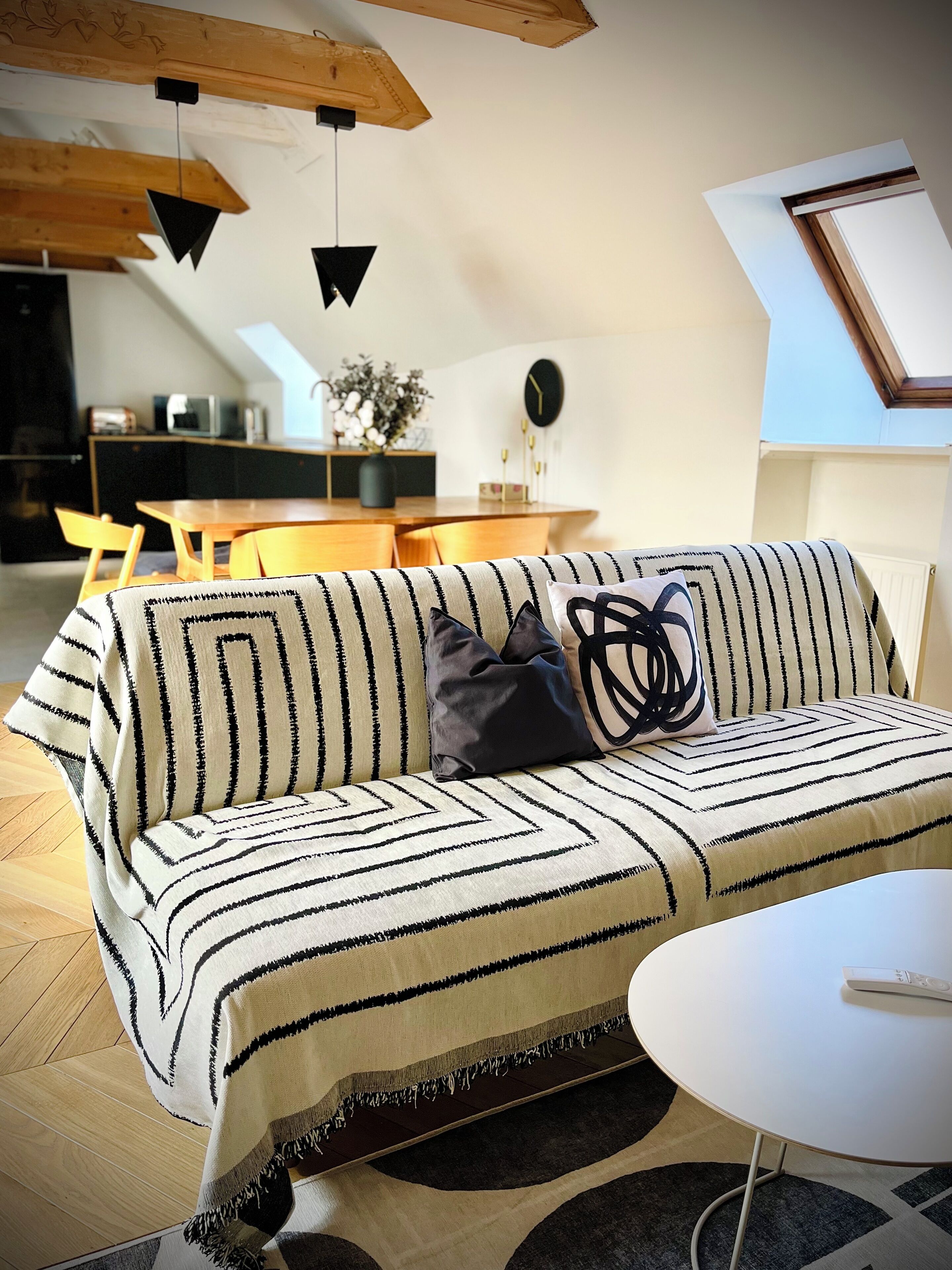 A modern living room with a striped sofa, a round coffee table, and a dining area in the background.