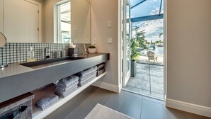Ein modernes Badezimmer mit einem großen Spiegel, einer Ablage mit Toilettenartikeln und Blick auf die Terrassenförmige Außengestaltung.