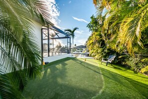 Un área exterior bien cuidada con césped artificial, una zona de estar y una estructura de vidrio.