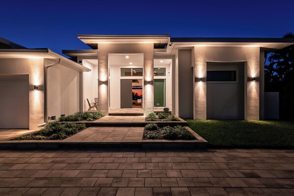 Een modern huis met een goed verlichte ingang, een overdekte veranda en een aangelegde voortuin.