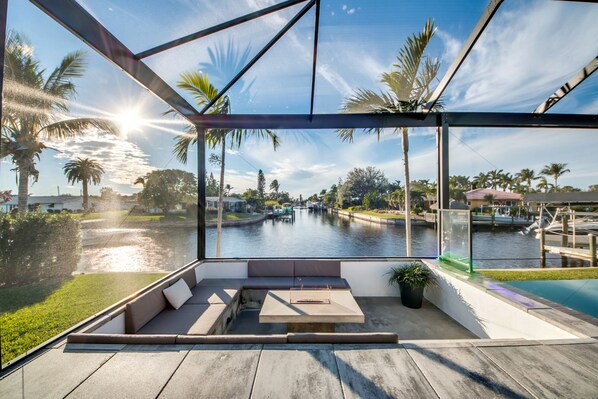 Un espacio exterior moderno con asientos y vistas a un canal y palmeras.