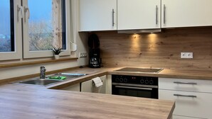 A modern kitchen with a wooden countertop, stainless steel sink, and white cabinets. - Vacation apartment Trockenbach (Riedenberg)