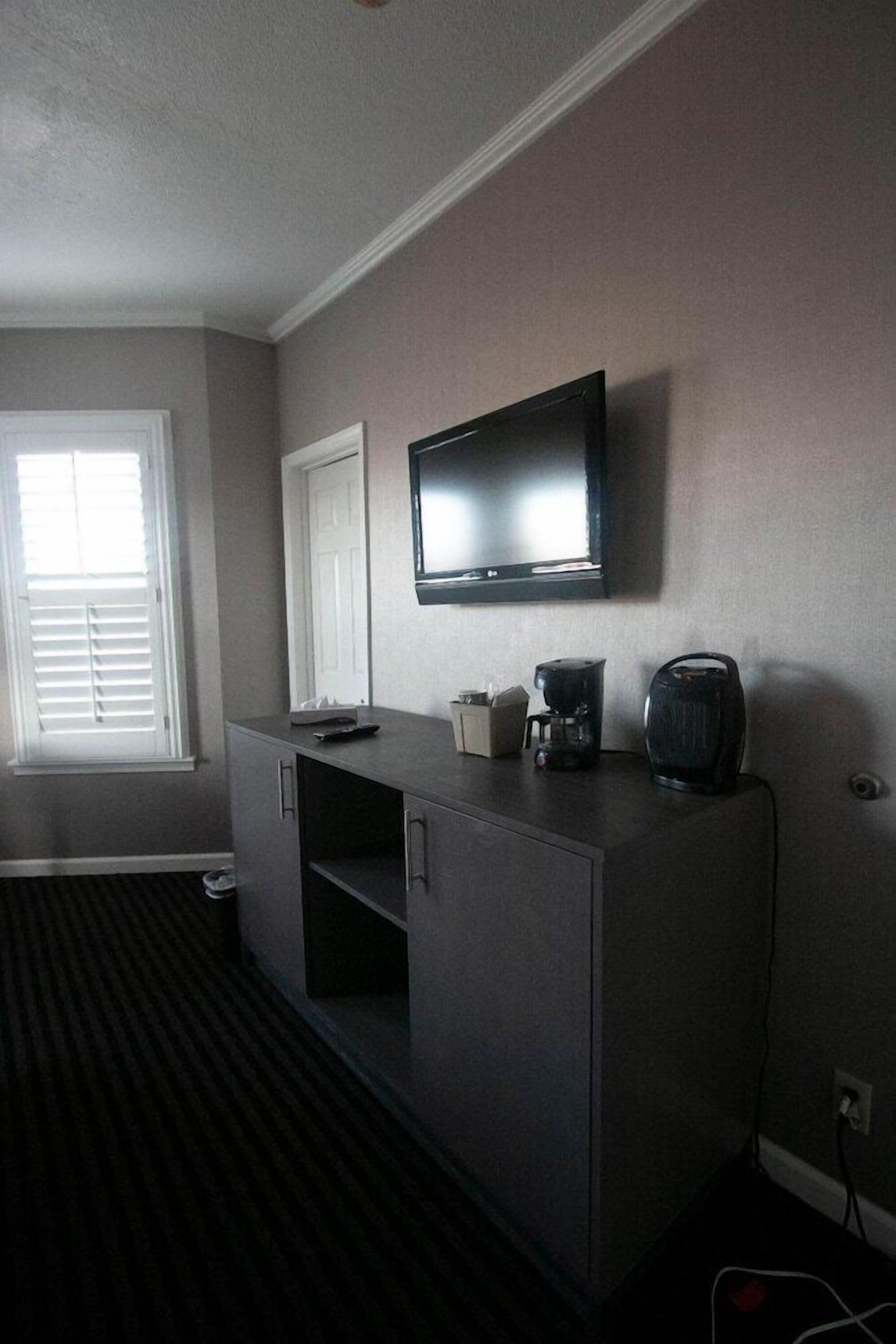 A room with a flat-screen TV mounted on the wall, a coffee maker, and a kettle on a counter.