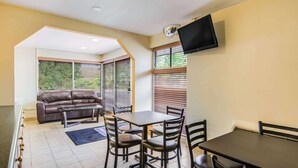 A dining area with a table and chairs, a sofa, and a TV mounted on the wall. - Econo Lodge near Richmond National Battlefield Park (Richmond)