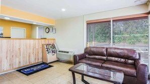 A reception area with a wooden reception desk, a brown leather sofa, a glass coffee table, and a window with blinds. - Econo Lodge near Richmond National Battlefield Park (Richmond)