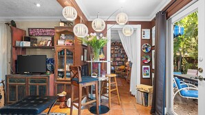 Ein gemütliches Wohnzimmer mit Fernseher, Bücherregalen, einem Couchtisch und einem Essbereich mit Stühlen und Tisch.