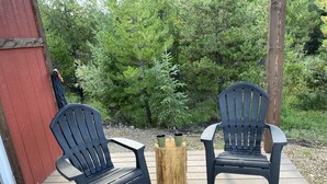 Dos sillas Adirondack sobre una terraza de madera, con un tocón y una jardinera de metal entre ellas.