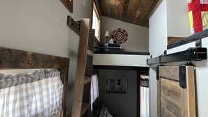 Una habitación rústica con vigas de madera, una cama litera, una mesita con una lámpara y un adorno en la pared.
