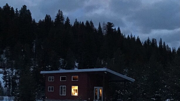 Una casa de dos pisos con el suelo cubierto de nieve, rodeada por un bosque.
