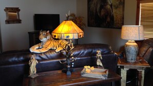 A living room with a leather sofa, a wooden coffee table, a tiger statue, a lamp, and a painting on the wall.