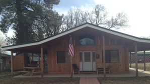 A wooden cabin with a covered porch, an American flag, and a gravel driveway.