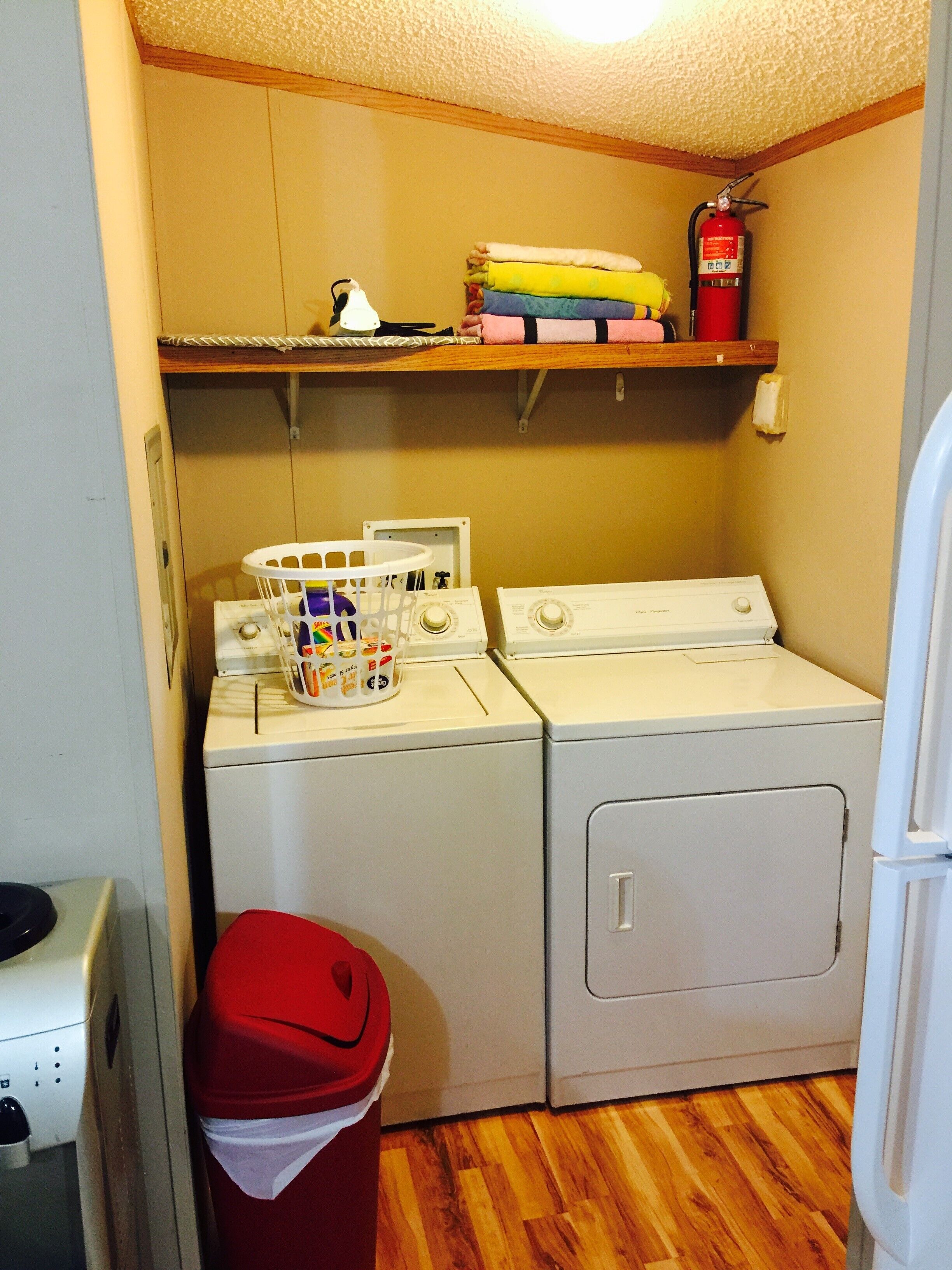 A laundry area with two washing machines, a dryer, a fire extinguisher, and a shelf with folded clothes.