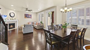 A spacious living area with a fireplace, a dining table with chairs, a sofa, and a ceiling fan.