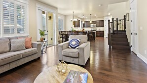 A spacious living room with a sofa, armchair, and coffee table. A kitchen and dining area are visible in the background.