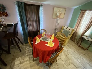 A dining area with a red tablecloth, wooden chairs, and a vase of flowers on the wall.