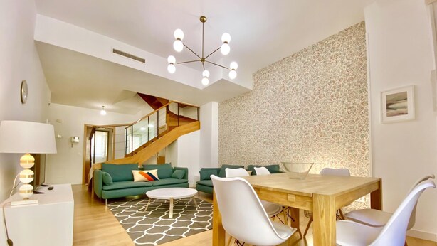 A modern living room with a wooden dining table, white chairs, a green sofa, and a patterned rug. - Opera, Duplex Apartment – Three-bedroom Duplex Apartment (Madrid)
