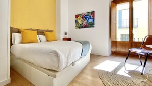 A bedroom with a bed, a chair, a colorful painting, and a view of a building through a door. - Opera, Duplex Apartment – Three-bedroom Duplex Apartment (Madrid)