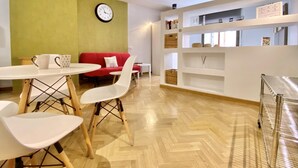 Uma sala de estar moderna com um sofá vermelho, cadeiras brancas, uma mesa redonda e um relógio na parede.